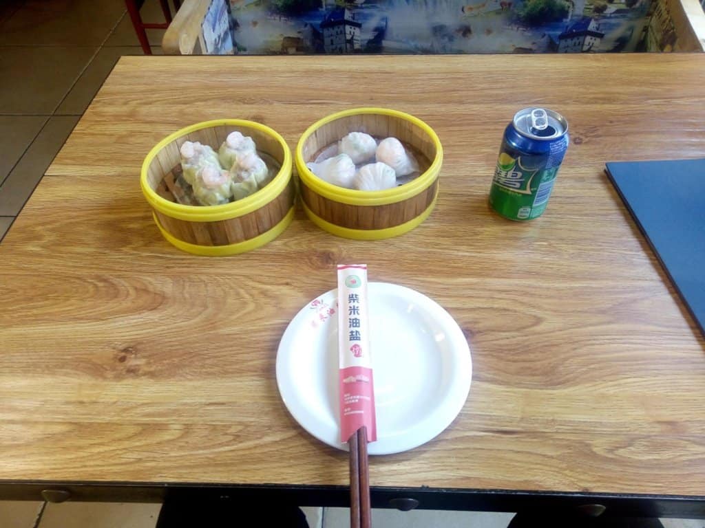 Authentic Chinese Dim sum from China. Shrimp dumplings and pork wrapped in yellow rice paper in bamboo bowls and steamers beside a sprite and in front of a plate topped with chopsticks