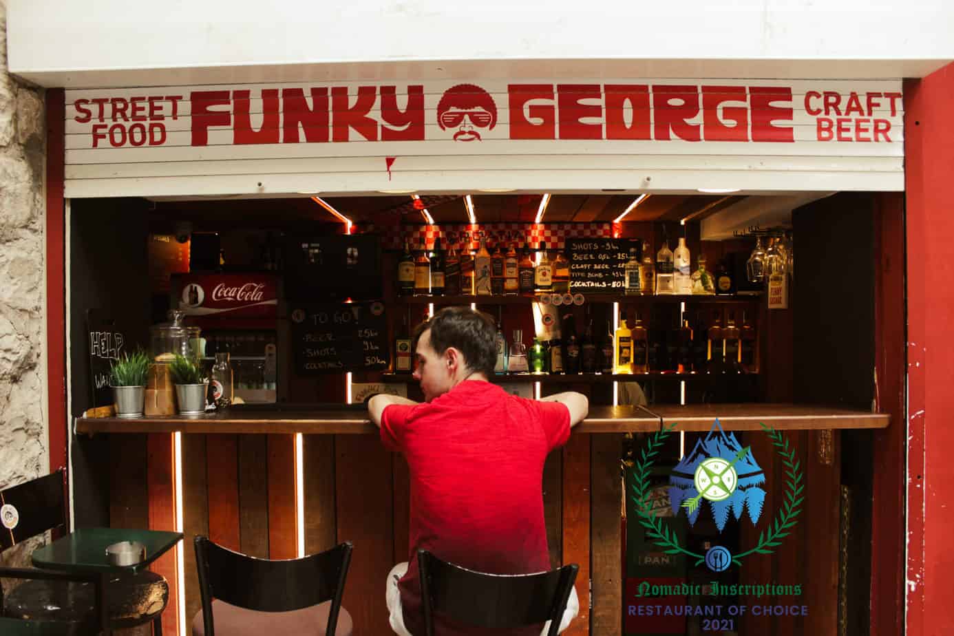 Funky George the first of our 2021 Restaurant of Choice winners. A man in red sits in front of the Funky George bar. The Funky george logo sits across the top.