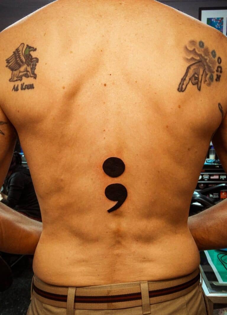 A Semicolon tattoo on the lower- middle back along the spine