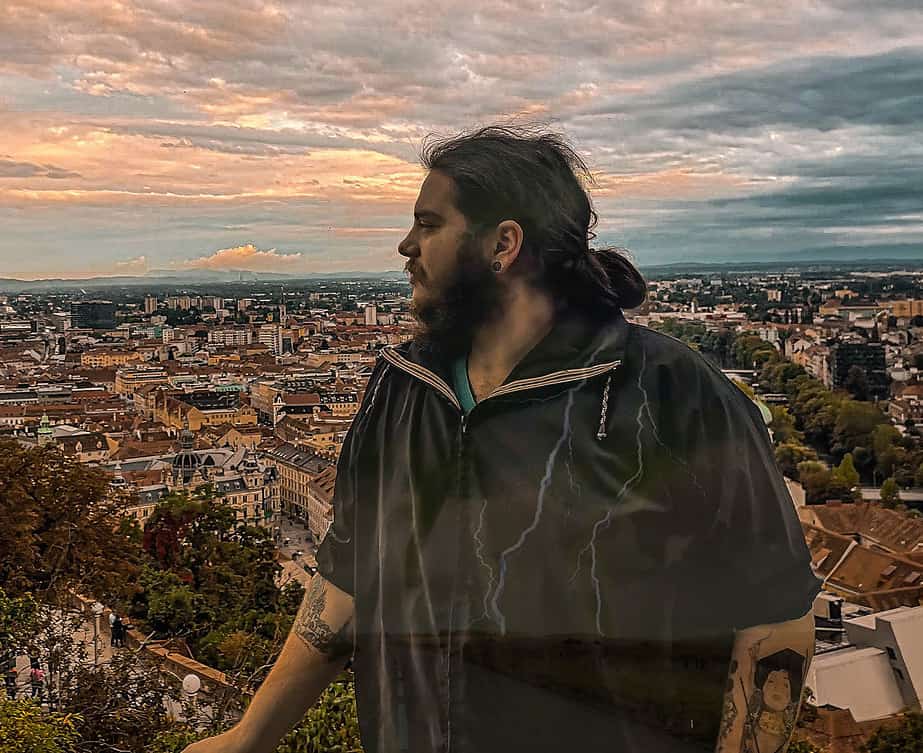 A picture of Jenson standing in front of a wide view of the City of Graz and looking on into the distance. The image of a tornado and lightning can be seen in his body, symbolizing rejection sensitive dysphoria and the turmoil it causes.